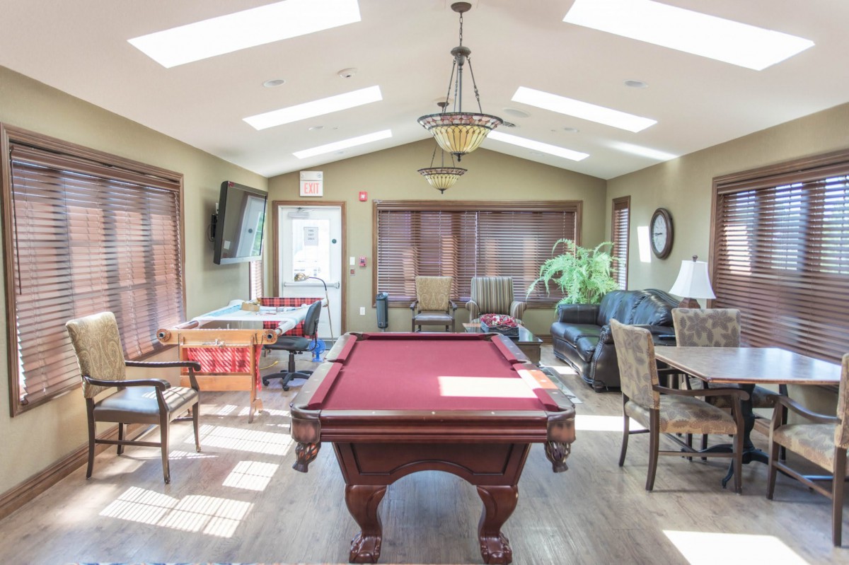 A cozy game room featuring a pool table and comfortable seating, illuminated by natural light from skylights.