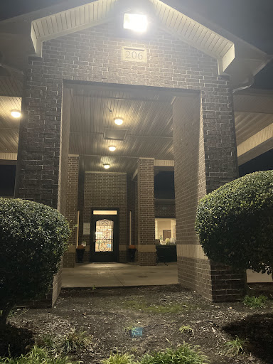 A well-lit entrance to a building at night, framed by neatly trimmed bushes.