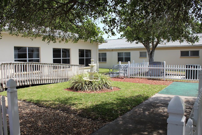 A modest building with a small garden, white fence, and surrounding trees.