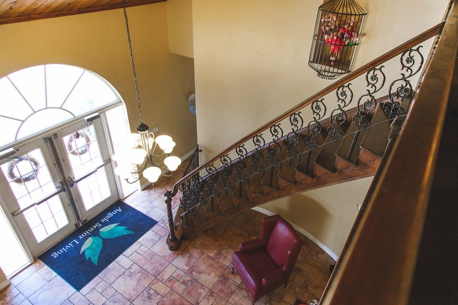 A view of a stylish foyer featuring a wrought iron staircase, elegant chandelier, and comfortable armchair.