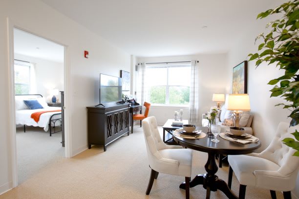 A bright and modern living room with a dining area, featuring elegant furniture and a large window.