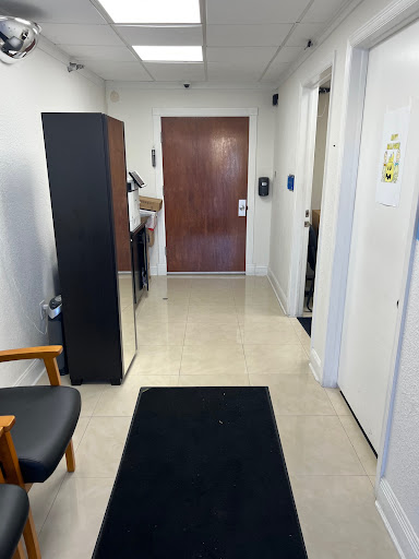 A view of a hallway in an office setting, showcasing a refrigerator and wooden door.