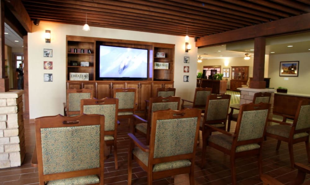 A cozy conference room with rows of wooden chairs facing a large television, surrounded by bookshelves.