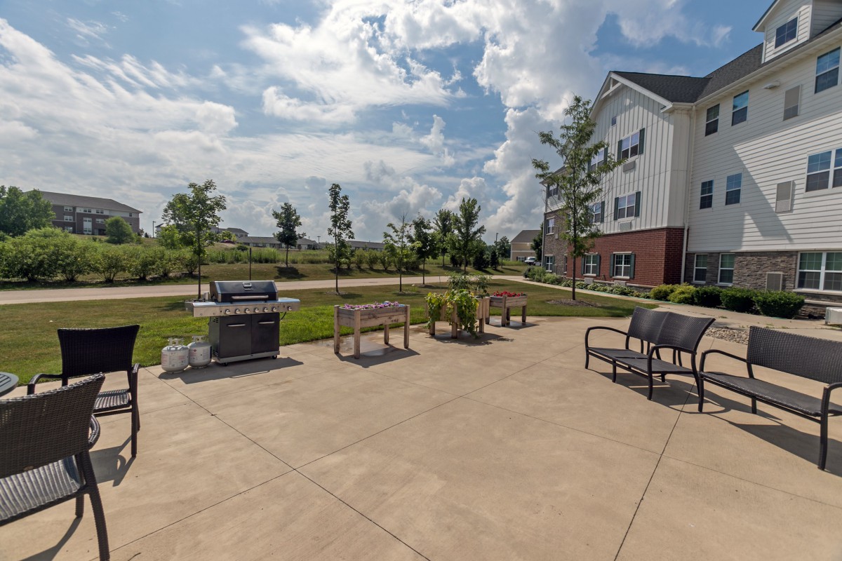 A sunny outdoor patio area featuring benches, grills, and a building in the background.