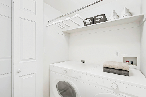 A clean and organized laundry room featuring a washing machine, dryer, and shelving for storage.