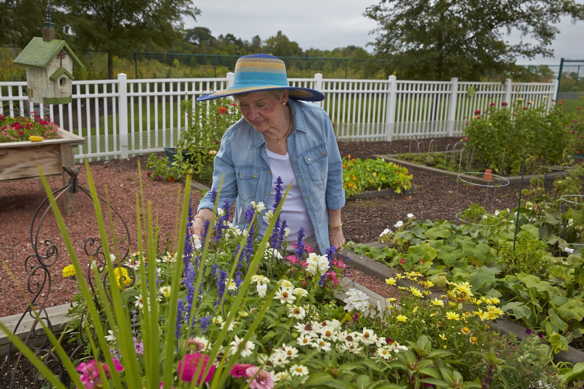 A woman tending to her garden, surrounded by colorful flowers and a white fence.