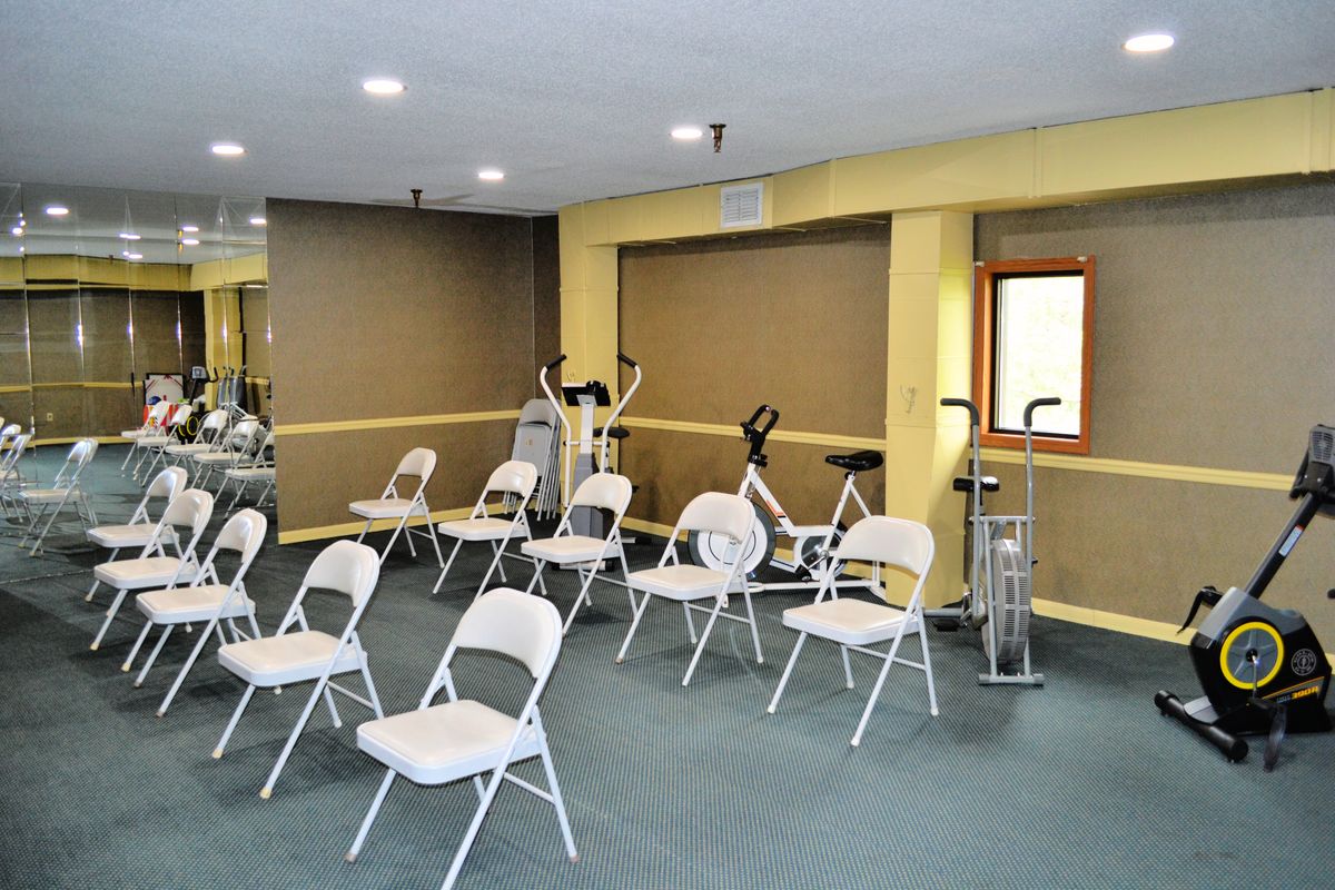 A room with folding chairs arranged for a meeting, featuring exercise equipment in the background.