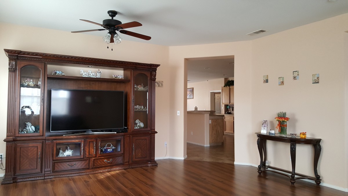 A cozy living room featuring a large entertainment center with a television, a ceiling fan, and hardwood flooring.