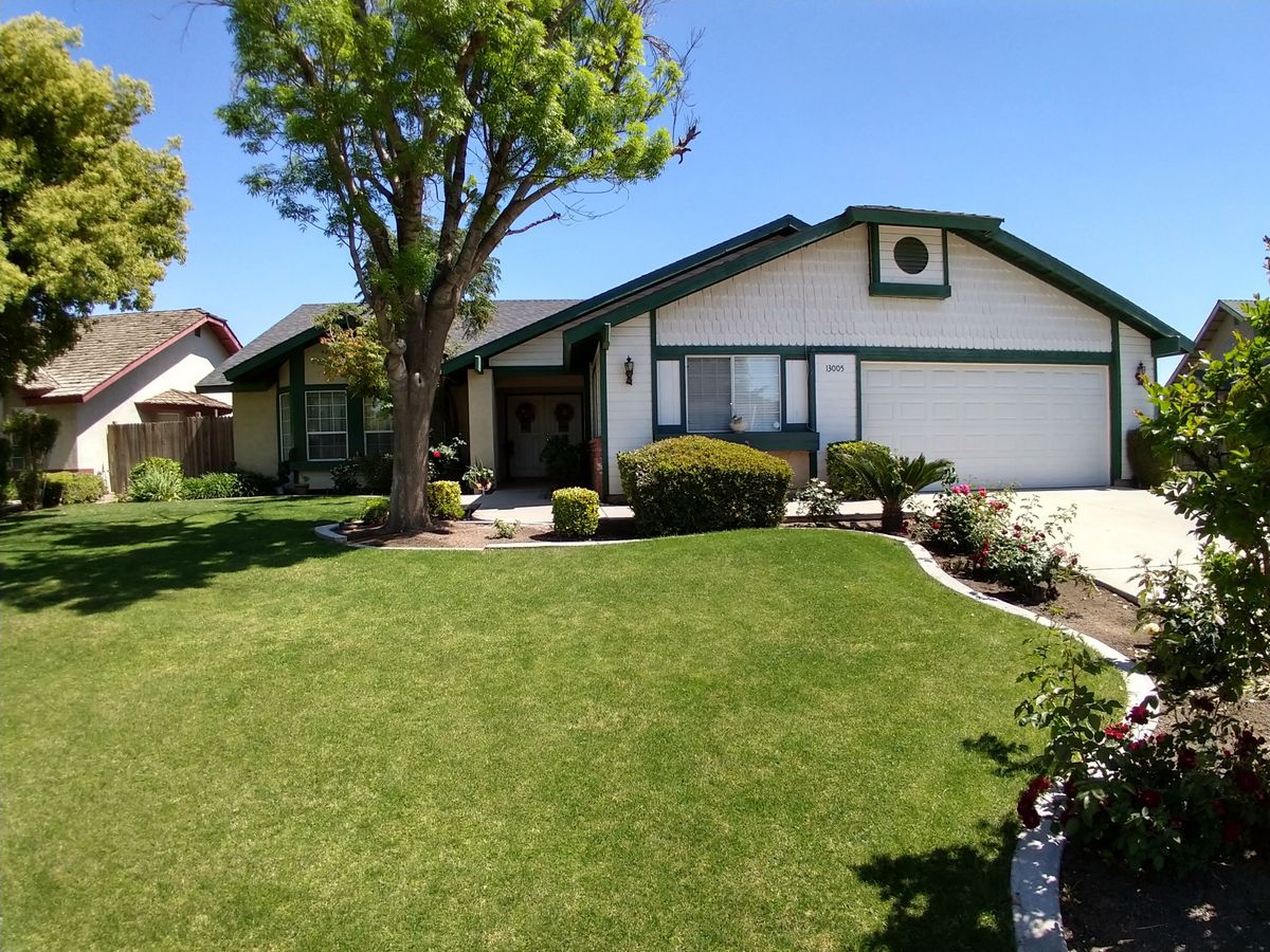 A suburban house with a well-maintained lawn and a large tree in the front yard.