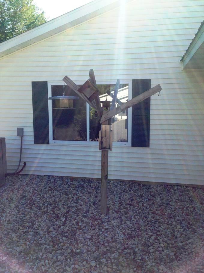 A wooden sculpture stands in front of a house, illuminated by sunlight.
