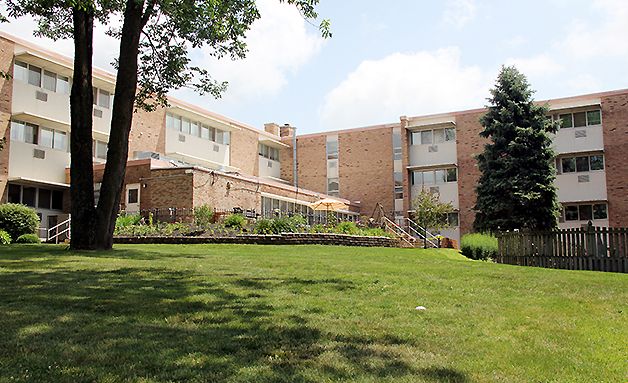 A brick apartment building with a well-maintained lawn and surrounding trees.
