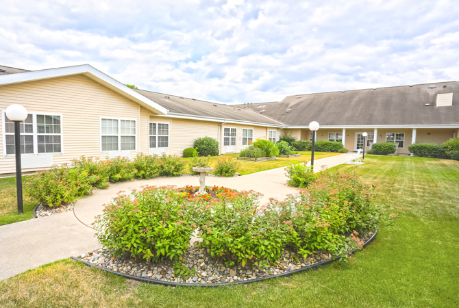 A one-story residential building with a landscaped garden and pathway under a cloudy sky.