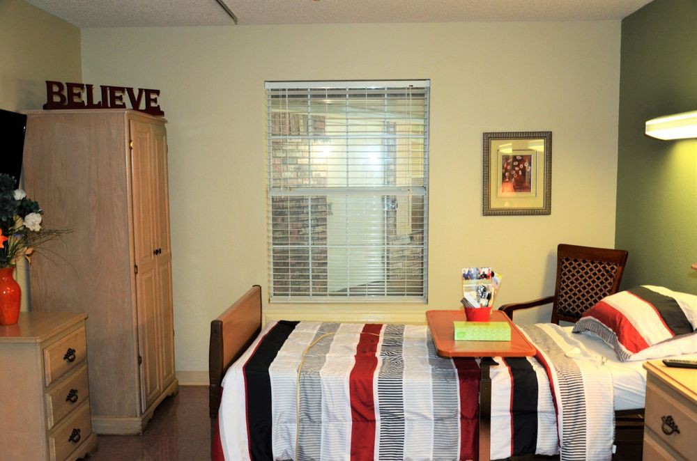 A neatly arranged bedroom with a striped bedspread, wardrobe, and a window with blinds.