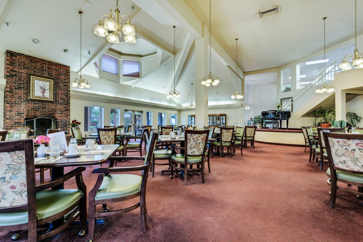 A spacious dining room with elegantly arranged tables and chairs, featuring large windows and chandeliers.