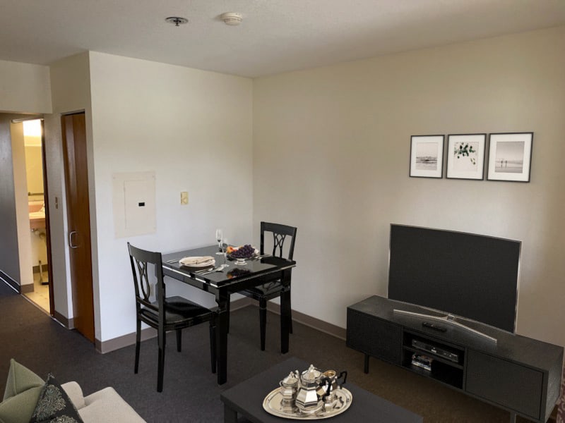 A cozy living and dining area with minimalist decor featuring a small dining table, chairs, sofa, and TV stand.