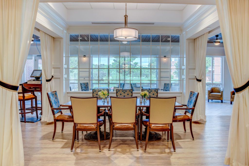 A spacious dining room with a large table and elegant chairs, featuring a chandelier and large windows.