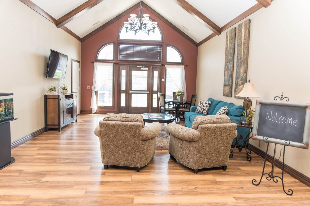 A spacious living room with elegant furniture and high ceilings, featuring cozy armchairs and a sofa on polished wood flooring.