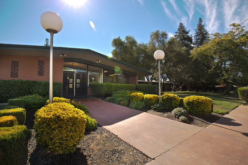 A welcoming entrance to a landscaped building, illuminated by natural sunlight.