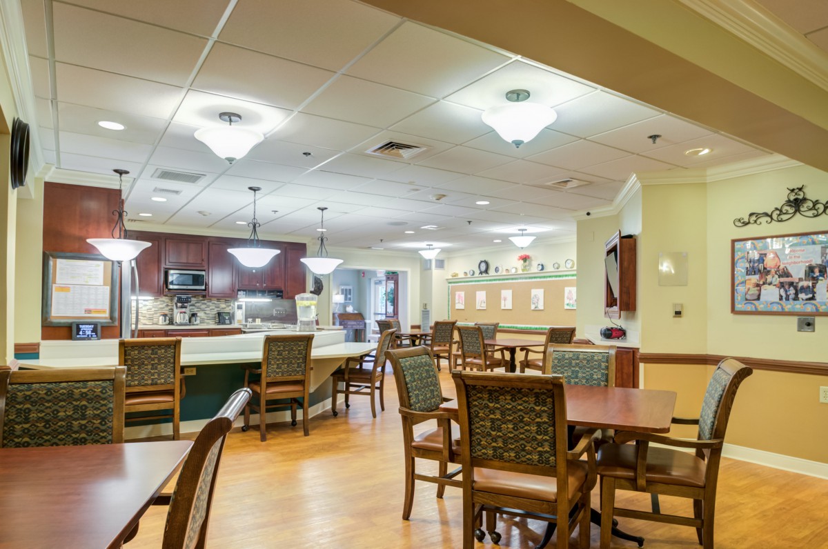 A well-lit dining area with tables and chairs, adjacent to a kitchen.