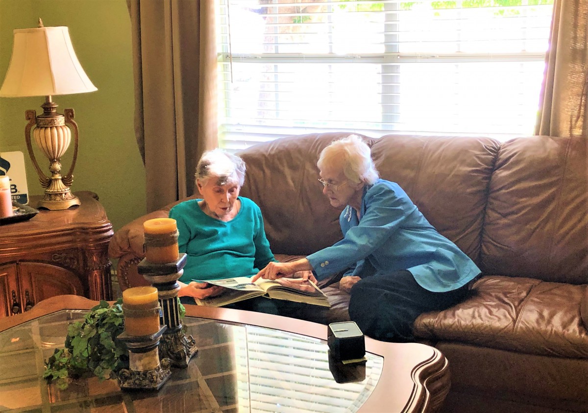 Two elderly individuals sitting on a couch, looking at a photo album in a cozy living room.