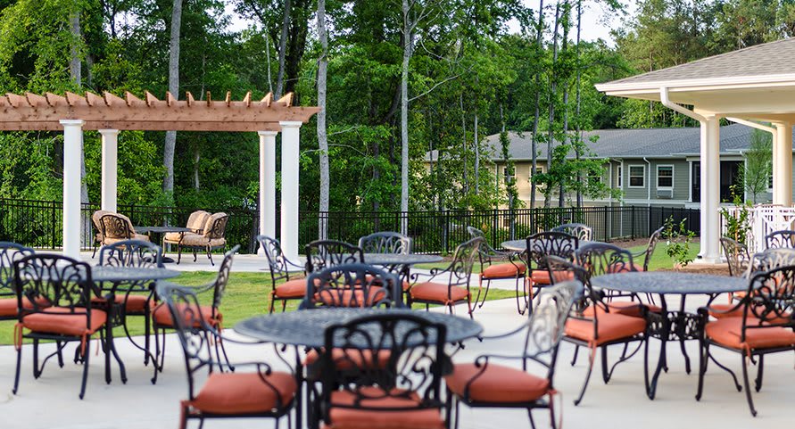 A serene outdoor patio area with tables, chairs, and a pergola surrounded by lush greenery.