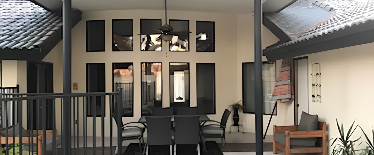 A modern patio area featuring a dining table set with chairs, large windows, and a ceiling fan.
