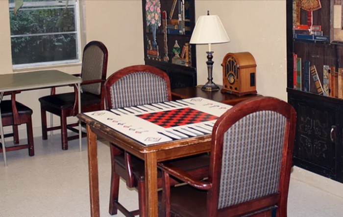 A cozy room setup with a table featuring a board game, surrounded by chairs and accented with a lamp and vintage radio.