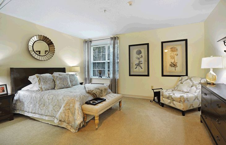 A well-decorated bedroom featuring a large bed, patterned bedding, framed artwork, and a cozy seating area by the window.
