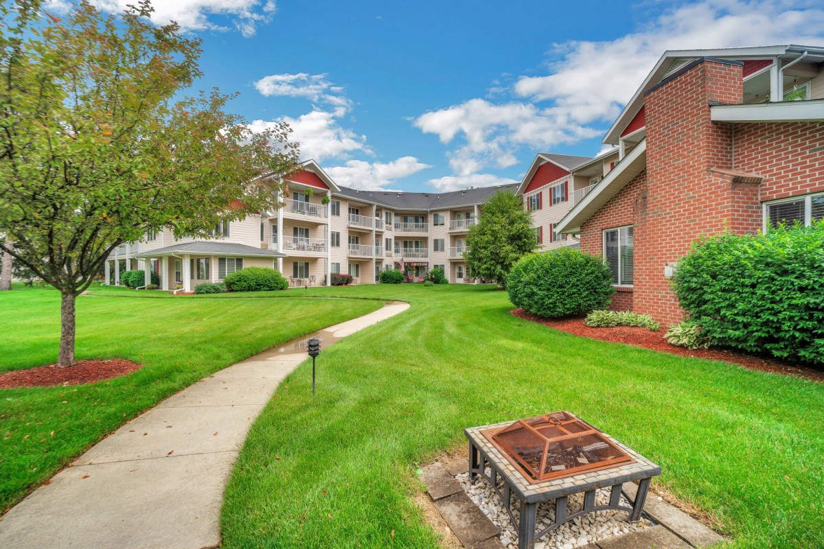 A well-maintained apartment complex with a lush green lawn and a central fire pit.