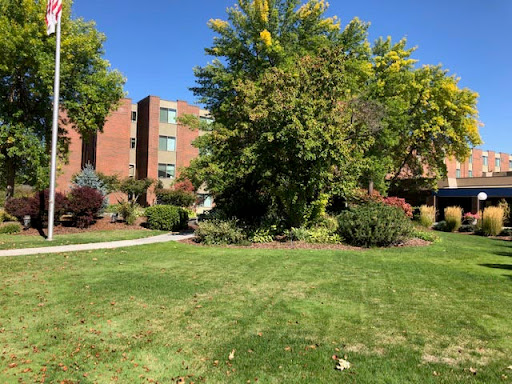 A serene view of a landscaped area featuring green grass, trees, and residential buildings under a clear blue sky.