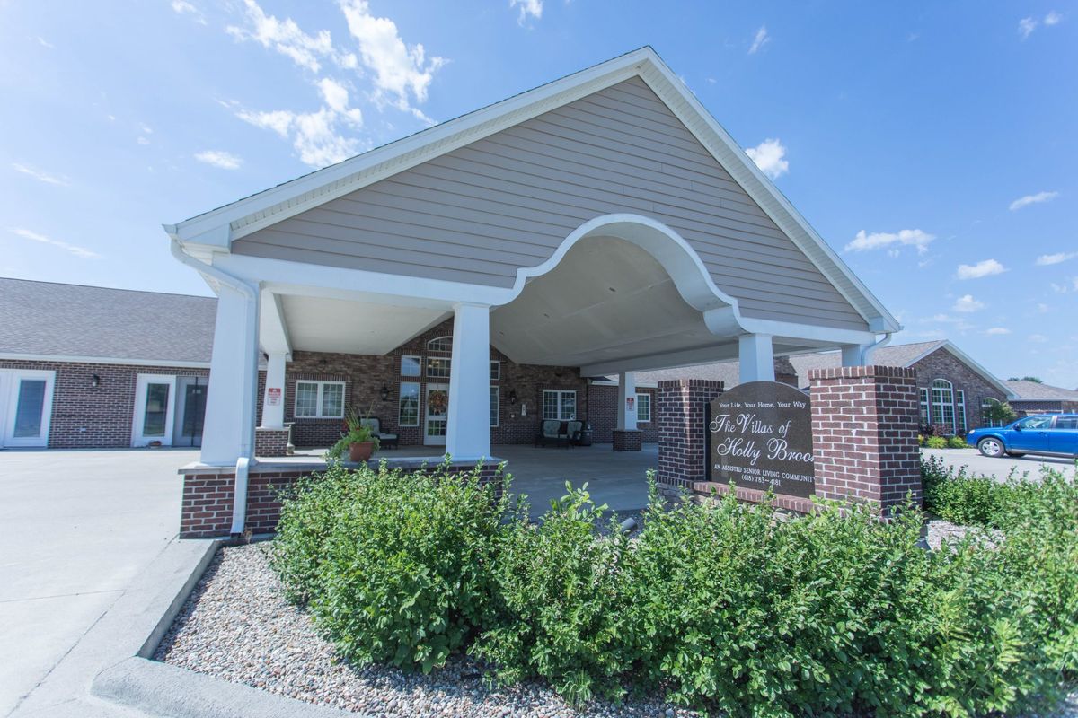 An entrance to a brick and siding building with landscaped greenery under a clear blue sky.