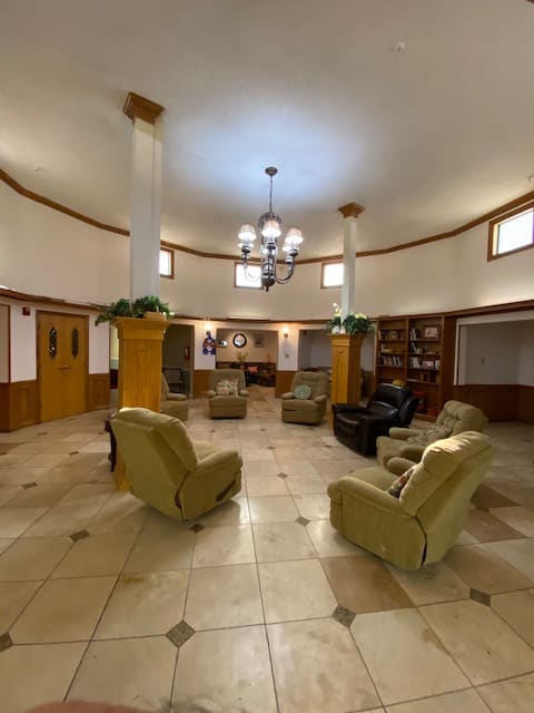 A spacious lobby with armchairs arranged in a circle, complemented by a chandelier and bookshelves.