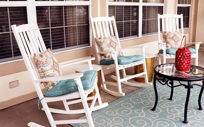Cozy porch with white rocking chairs, colorful cushions, and a patterned rug.