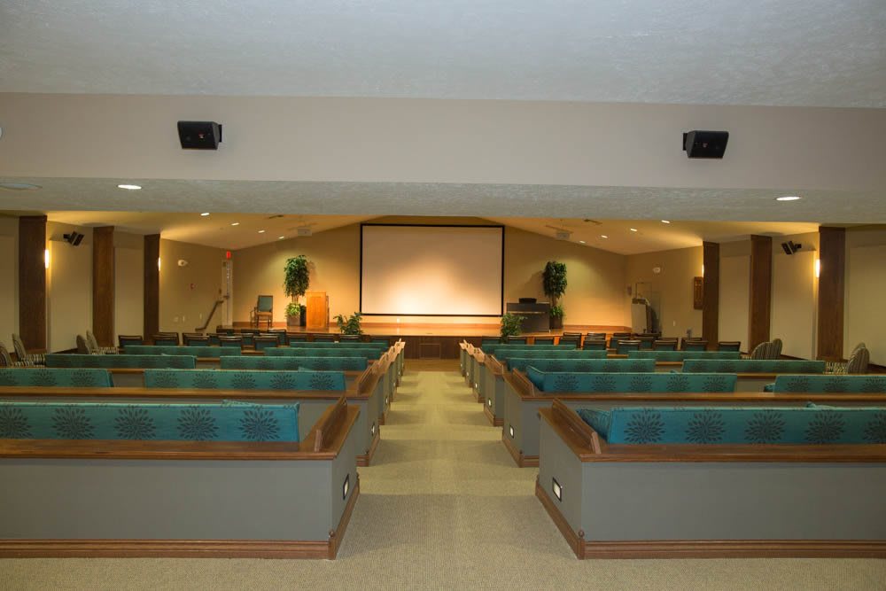 An empty auditorium with rows of seats facing a projection screen and stage.
