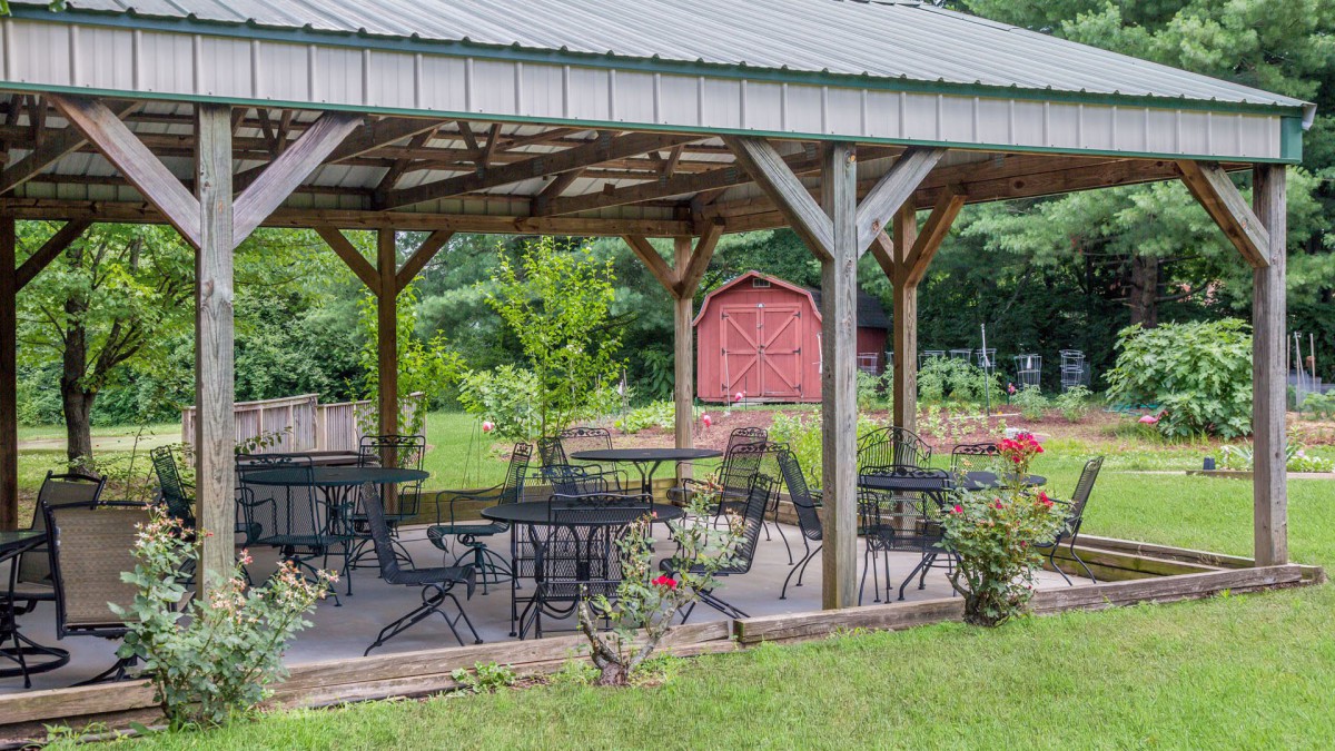 A wooden gazebo with tables and chairs surrounded by lush greenery.