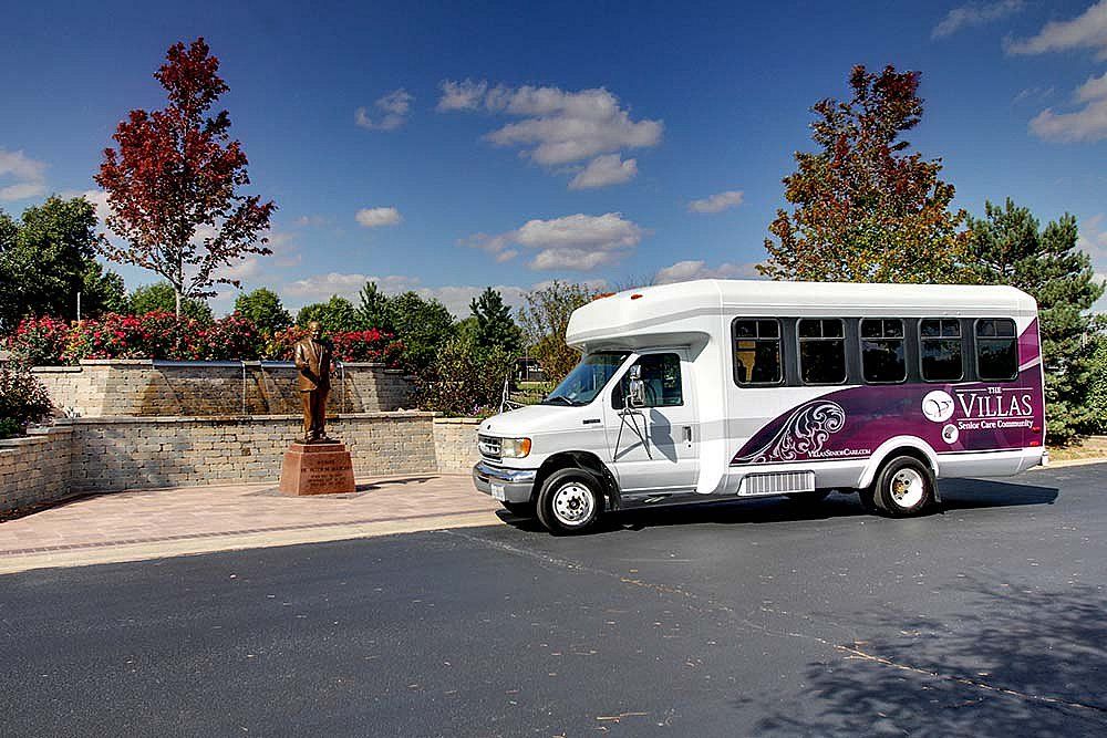 A white and purple shuttle bus parked on the side of a road under a clear blue sky.