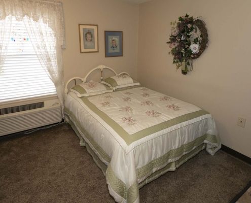 A cozy bedroom featuring a neatly made bed with a decorative quilt, adorned with wall art and curtains.