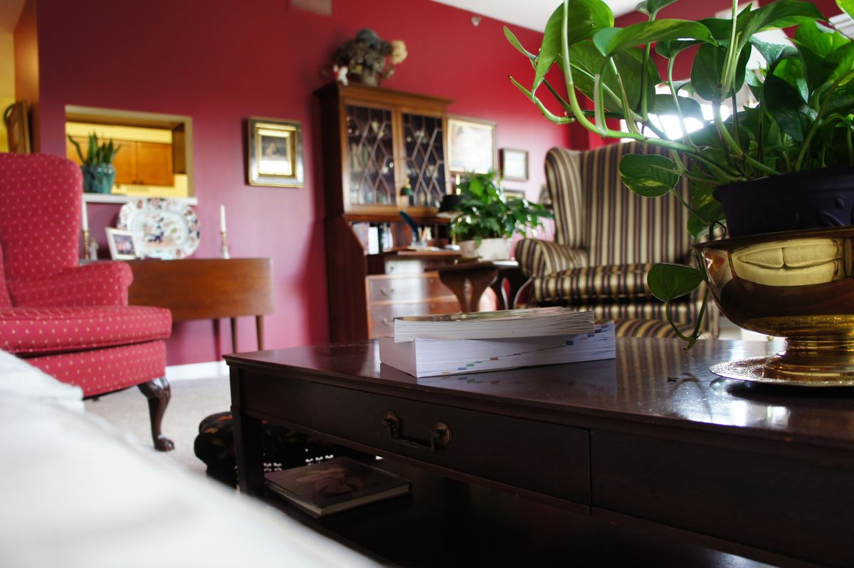 A cozy living room with red walls, featuring a wooden coffee table, wingback chair, and decorative plants.