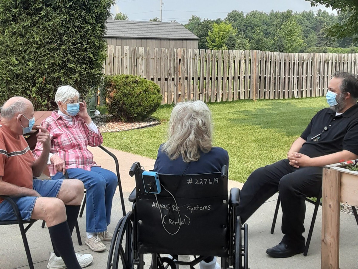 A group of people having a conversation in a garden setting, with one person in a wheelchair.