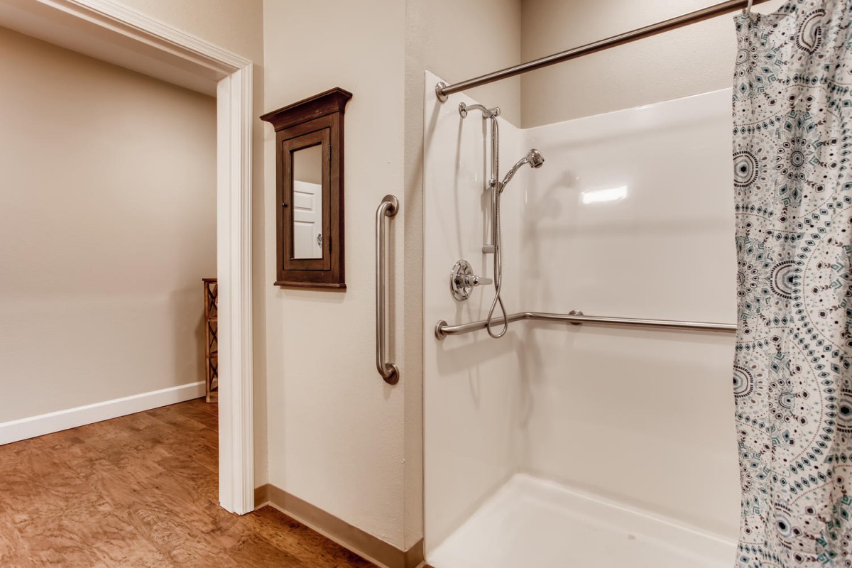 An accessible bathroom featuring a shower with grab bars and a handheld showerhead.