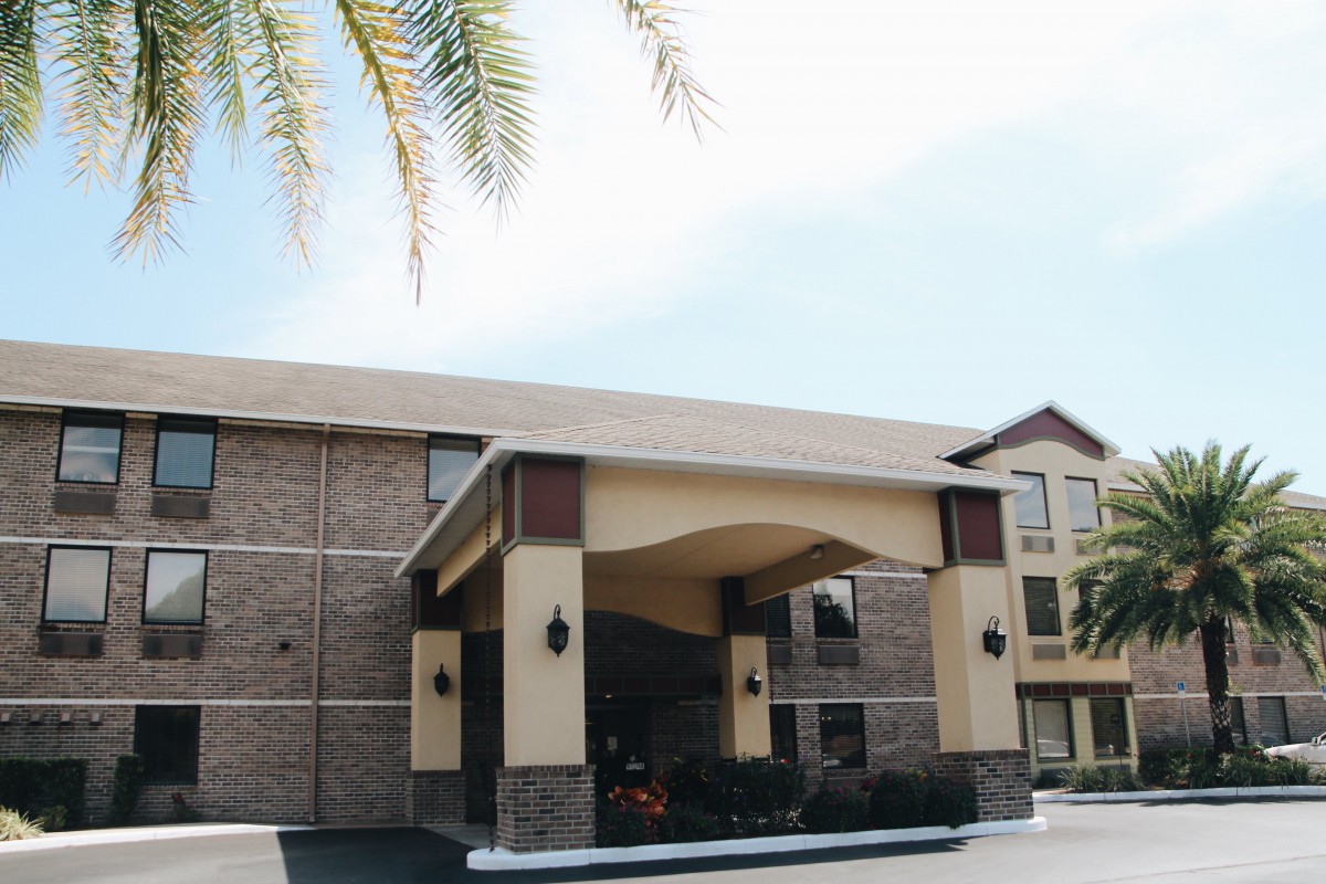 The exterior of a hotel with a covered entrance and palm trees nearby.
