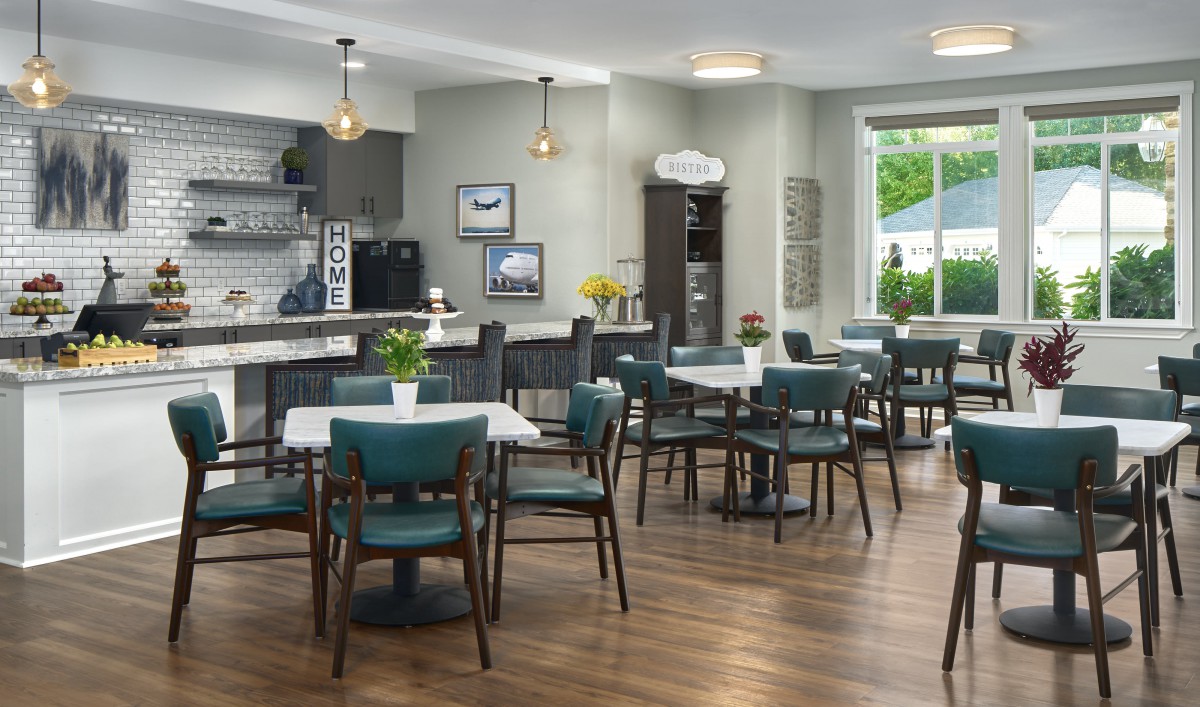A modern cafe interior with wooden floors, teal chairs, and ample natural light.