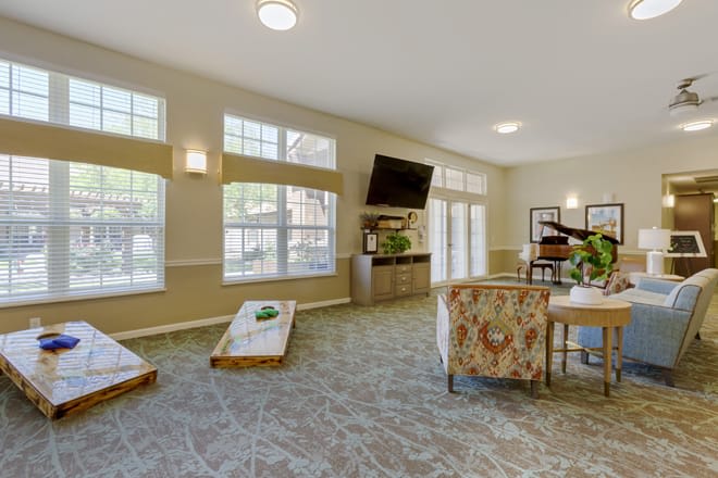 A spacious and well-lit living room featuring comfortable seating, a mounted television, and an indoor cornhole game setup.