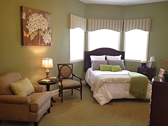 A cozy bedroom with green walls, featuring a bed, armchair, and lamp.
