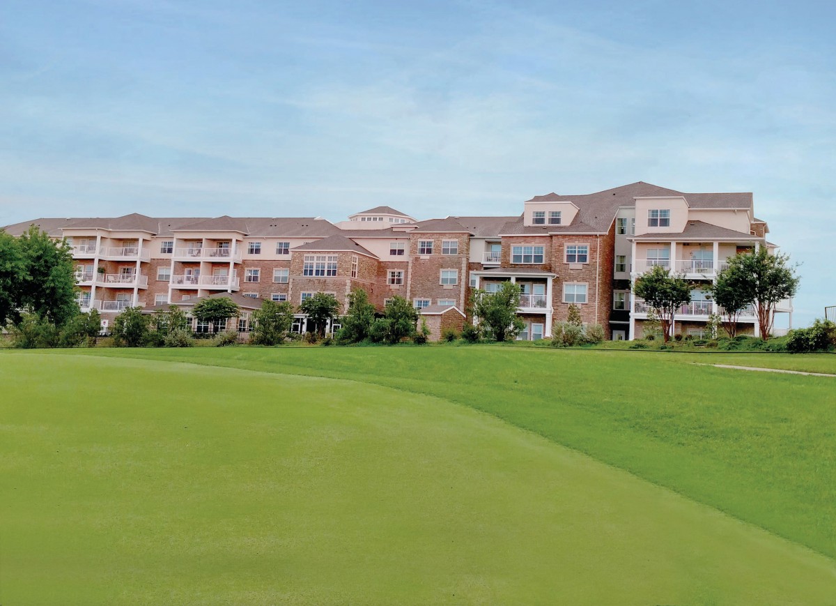 A scenic view of a large building next to a lush golf course under a clear sky.