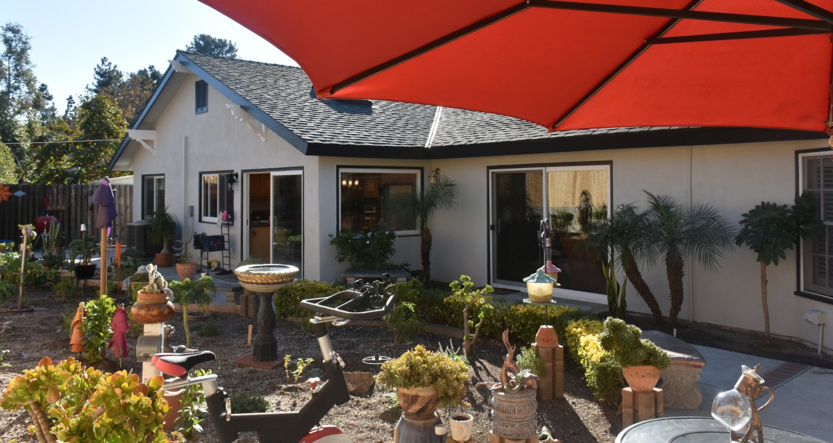 A sunny backyard garden with a patio and red umbrella.