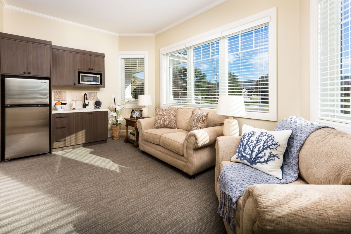 A cozy and well-lit living room featuring comfortable sofas, large windows with blinds, and modern decor elements.