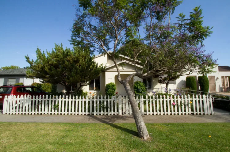 A suburban house with a white picket fence and a tree in the front yard.