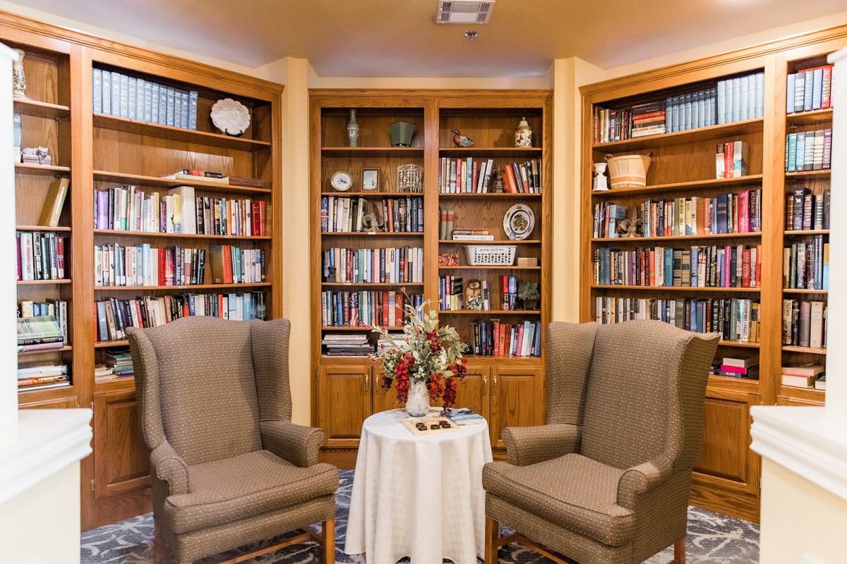 A cozy reading nook with two chairs and a table surrounded by bookshelves.