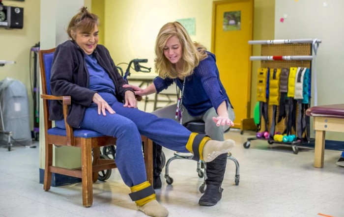 A physical therapist assists an elderly woman with leg exercises in a rehabilitation center.